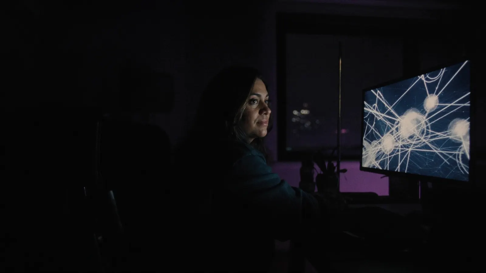 Una ingeniera trabaja de noche frente a un monitor con un diagrama de nodos